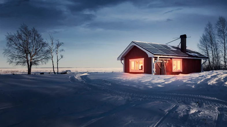 Rött fritidshus med solceller på taket. Vinter med mycket snö. Skoterspår i snön. 